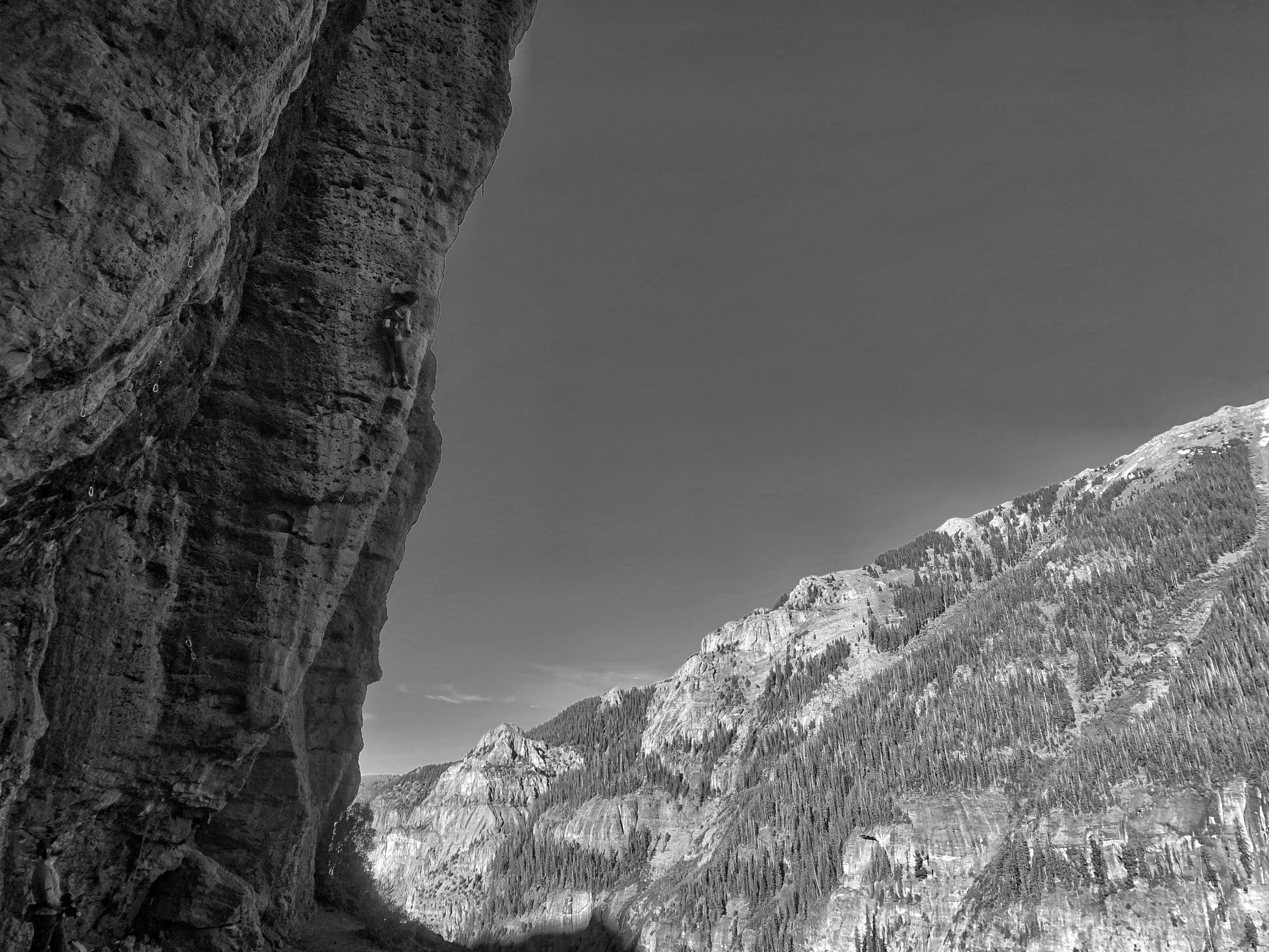 Black and white photo of a female climber on a steep arete climb with mountains in the background