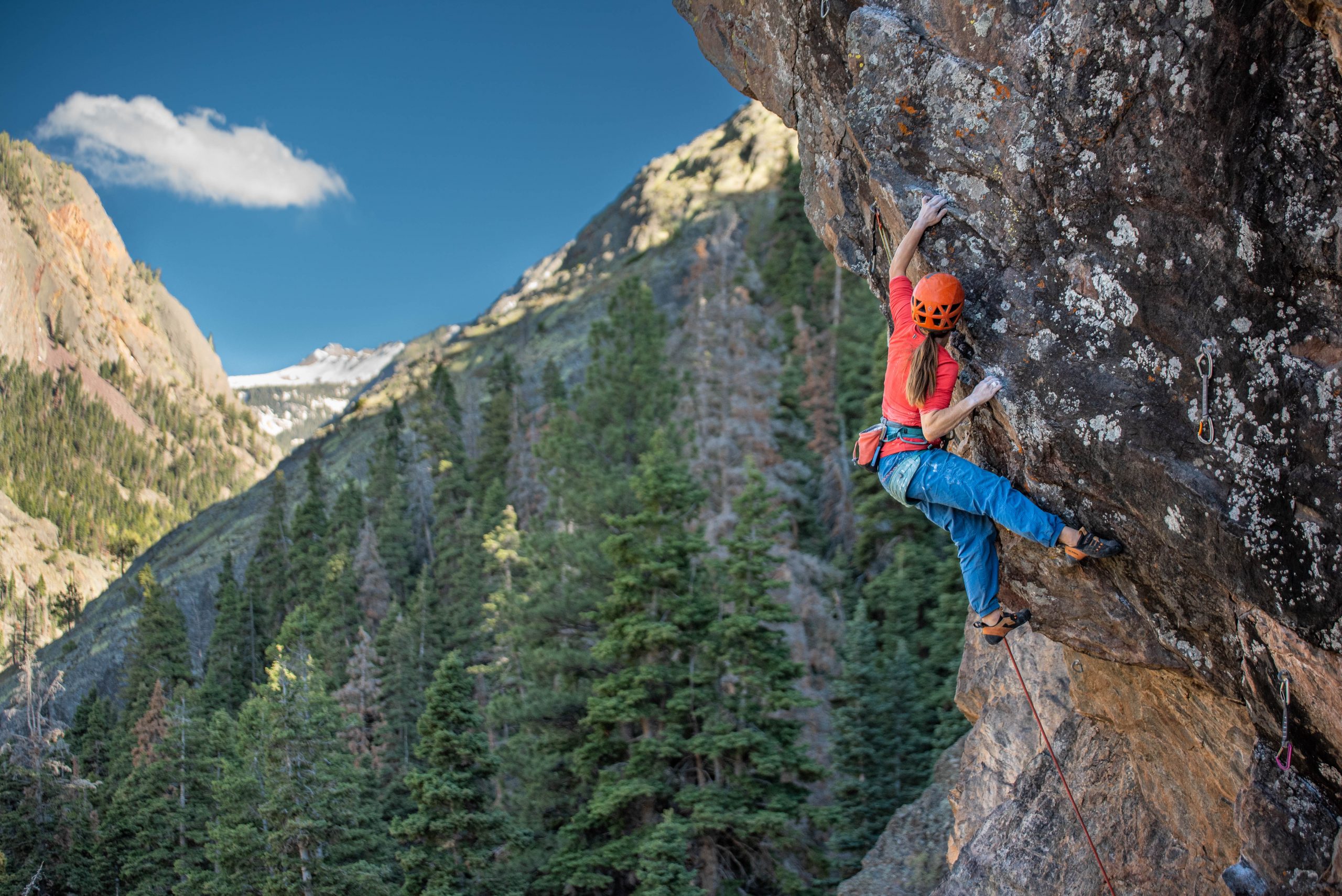 A photo of a woman climbing an overhanging bolted arête with mountains in the background.